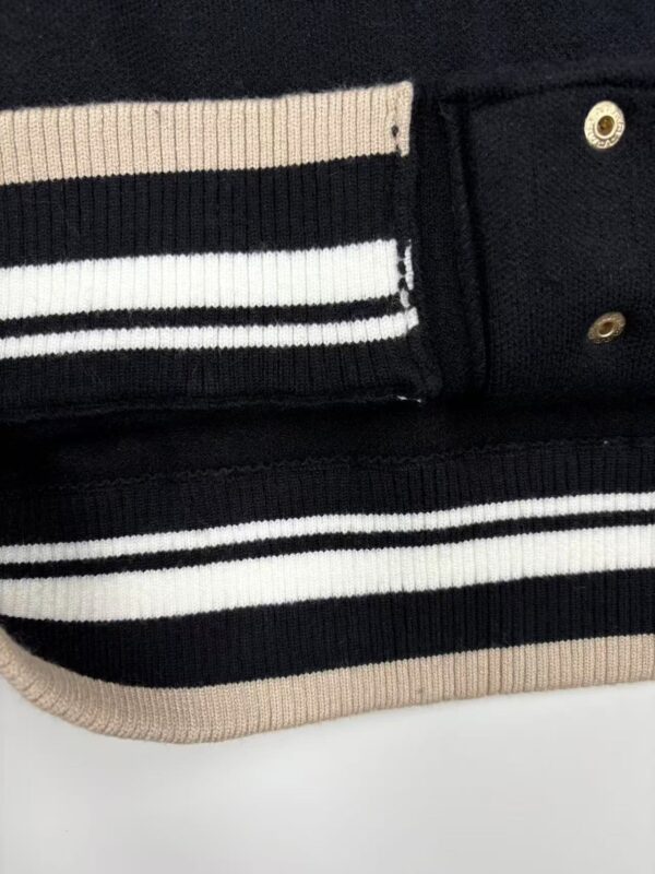 Close-up of black and beige striped knitwear fabric with gold button details, showcasing high-quality craftsmanship and stylish design.