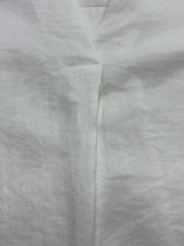 Detailed close-up of a white fabric seam, showcasing fine stitching and smooth texture, ideal for fashion and textile product descriptions.