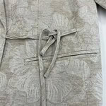 Close-up of a beige linen blazer with a tied waist belt, showcasing its textured fabric and tailored design, perfect for stylish casual or office wear.