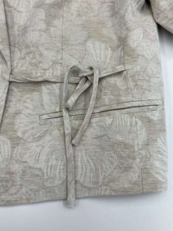 Close-up of a beige linen blazer with a tied waist belt, showcasing its textured fabric and tailored design, perfect for stylish casual or office wear.