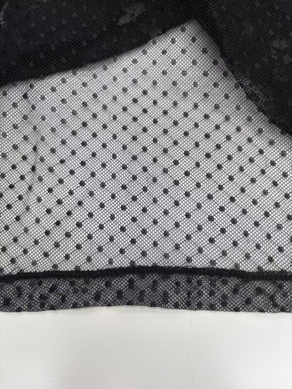 Close-up of black and white polka dot fabric with textured pattern, ideal for fashion and clothing design.