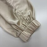 Close-up of a beige satin sleeve with gathered elastic cuff, showcasing smooth texture and luxurious finish, ideal for fashion and clothing design.