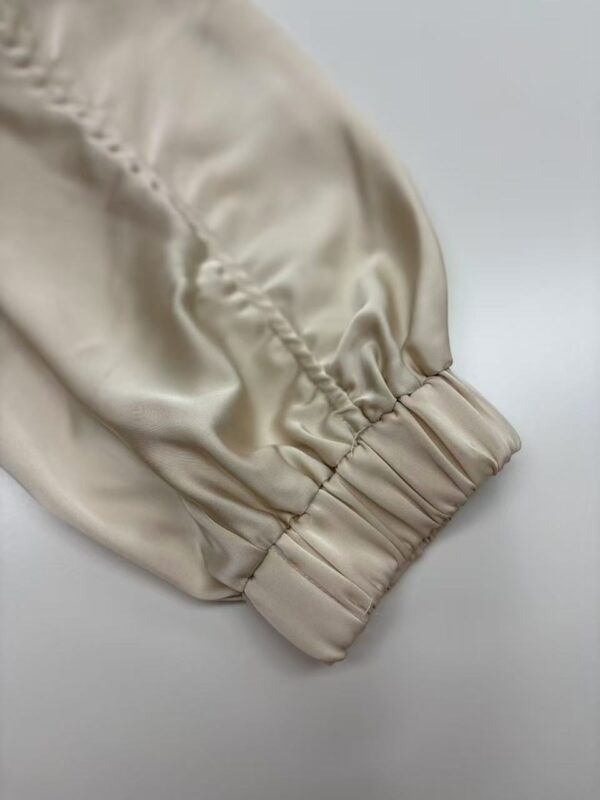 Close-up of a beige satin sleeve with gathered elastic cuff, showcasing smooth texture and luxurious finish, ideal for fashion and clothing design.