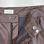 Close-up of a brown leather skirt with zipper and button details, showcasing high-quality craftsmanship and trendy fashion style.