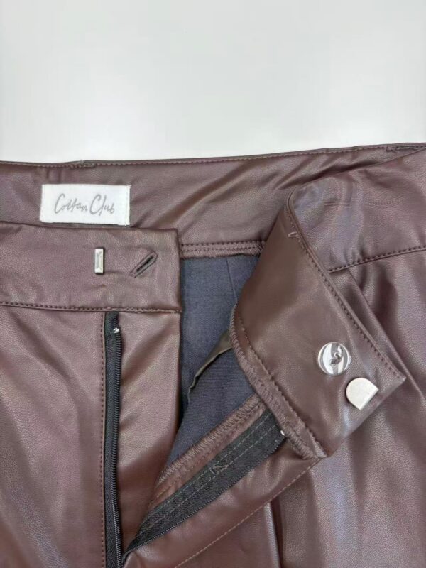 Close-up of a brown leather skirt with zipper and button details, showcasing high-quality craftsmanship and trendy fashion style.