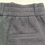 Close-up of stylish grey textured women's trousers with detailed waistband and tailored fit, perfect for professional or casual wear.