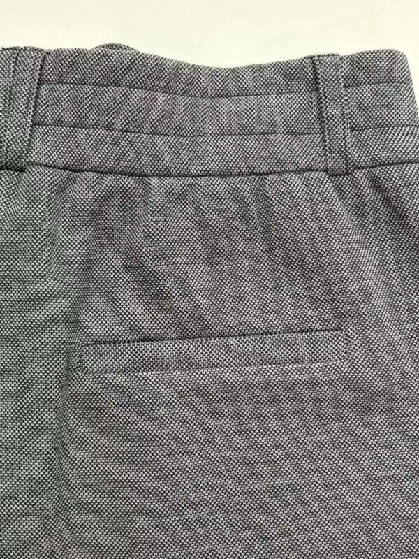 Close-up of stylish grey textured women's trousers with detailed waistband and tailored fit, perfect for professional or casual wear.