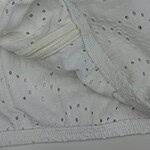 Close-up of white fabric with small eyelet holes and a zipper detail, showcasing delicate textile design and craftsmanship.