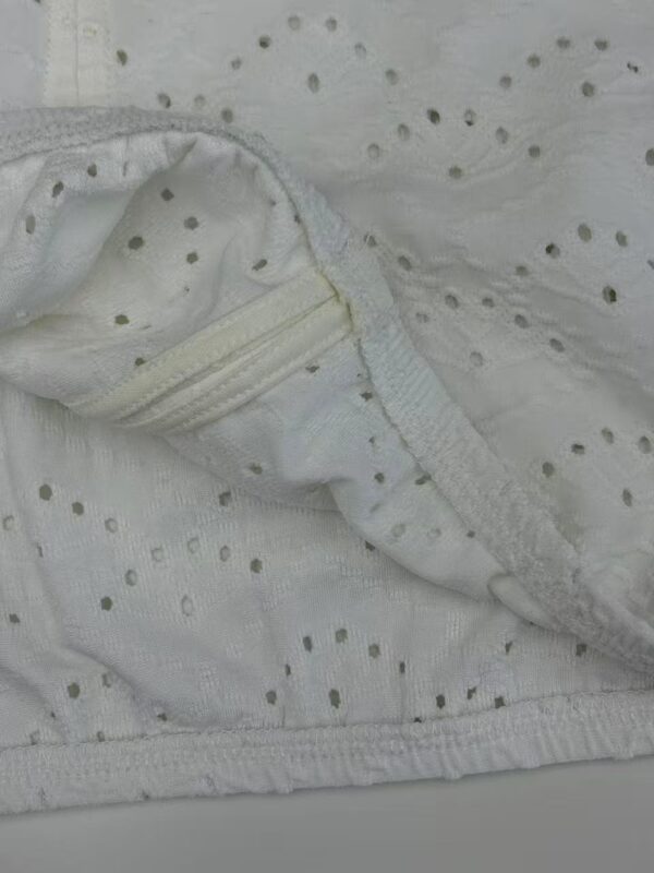 Close-up of white fabric with small eyelet holes and a zipper detail, showcasing delicate textile design and craftsmanship.