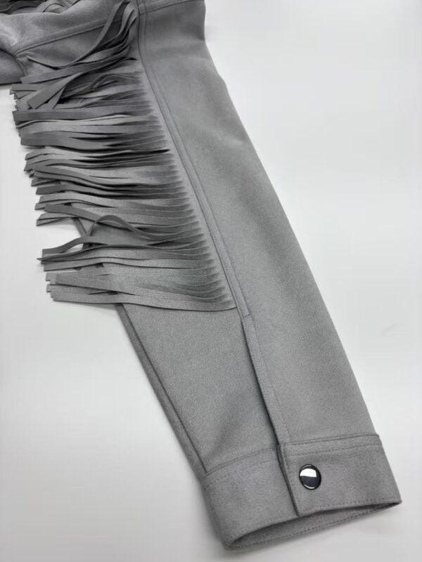 Close-up of a grey dress with fringe detailing on the sleeve, showcasing stylish and modern fashion design.