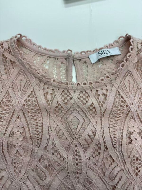Close-up of a pink lace dress with intricate patterns and a keyhole back closure, perfect for stylish occasions.