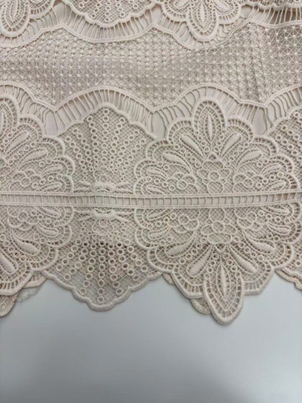Close-up of intricate beige lace fabric with detailed embroidery and patterns, ideal for fashion and wedding dress design.