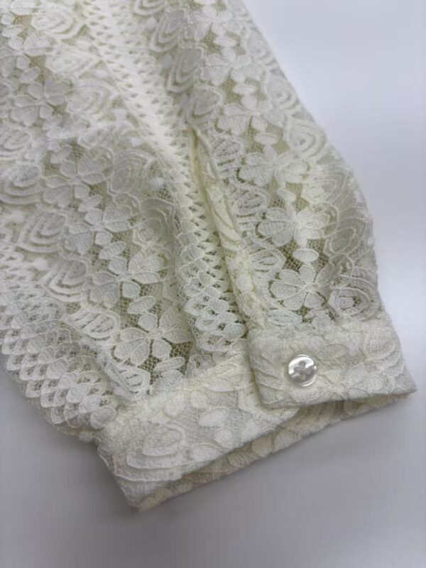 Close-up of an elegant ivory lace sleeve with a pearl button, showcasing intricate floral lace pattern and delicate craftsmanship.