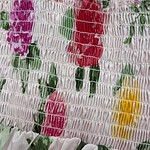 Close-up of a floral smocked dress with pink, red, yellow, and green flowers on a light background, showcasing detailed stitching and vibrant colors.