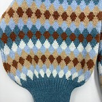 Close-up of a knitted sweater with a colorful argyle pattern in shades of blue, brown, beige, and white, featuring a ribbed teal cuff.