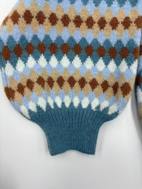 Close-up of a knitted sweater with a colorful argyle pattern in shades of blue, brown, beige, and white, featuring a ribbed teal cuff.