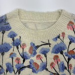 Close-up of a women's sweater with a floral pattern featuring blue, pink, and orange flowers on a cream background.