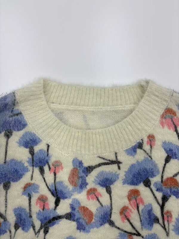 Close-up of a women's sweater with a floral pattern featuring blue, pink, and orange flowers on a cream background.