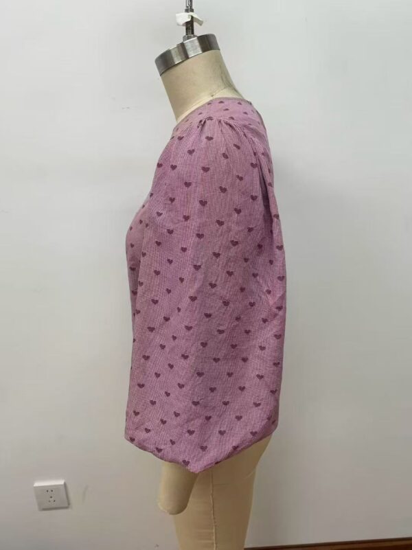 Pink women's blouse with small heart patterns, featuring a round neckline and puffed sleeves, displayed on a mannequin.