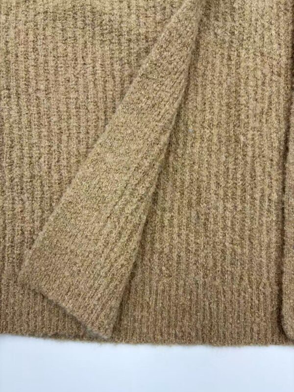 Close-up of a beige knitted sweater with a folded sleeve, showcasing soft texture and fine ribbing, perfect for fall and winter fashion.