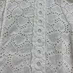 Close-up of white eyelet lace fabric with heart-shaped cutouts and embroidered details, showcasing intricate craftsmanship and delicate design.