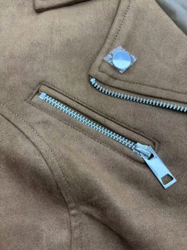 Close-up of a beige jacket featuring a silver zipper and a decorative button, highlighting fashion and clothing details.