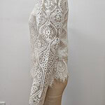 Close-up of a white lace dress with intricate floral patterns, long sleeves, and scalloped edges, displayed on a mannequin against a plain background.