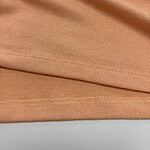 Close-up of peach-colored fabric showing smooth texture and fine stitching details, ideal for fashion and apparel design.