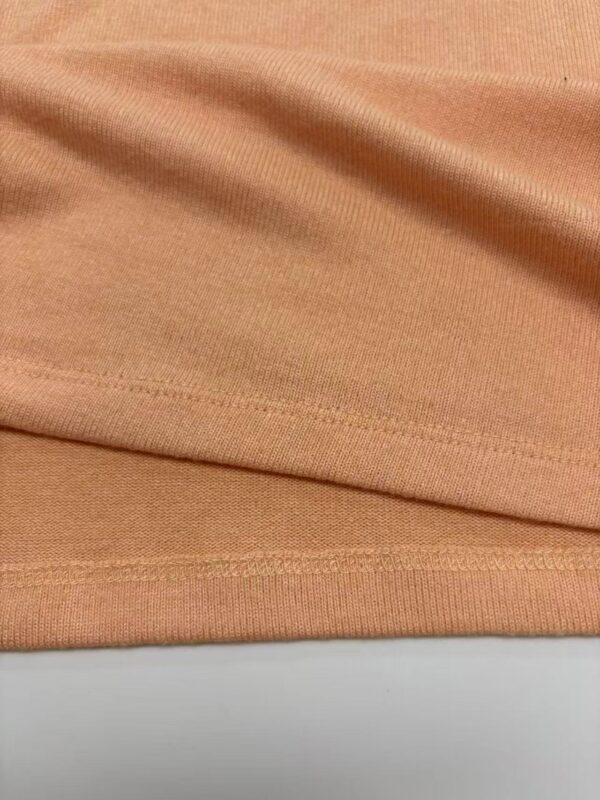 Close-up of peach-colored fabric showing smooth texture and fine stitching details, ideal for fashion and apparel design.