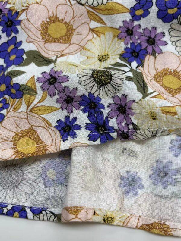 Close-up of floral fabric with pink, purple, white, and yellow flowers, suitable for fashion and textile projects.