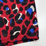 Close-up of vibrant leopard print fabric with red, black, white, and blue spots, showcasing a stylish and bold pattern for fashion apparel.