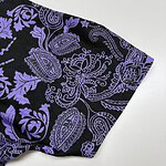 Close-up of black fabric with intricate purple paisley and floral patterns, showcasing detailed textile design for fashion or home decor.