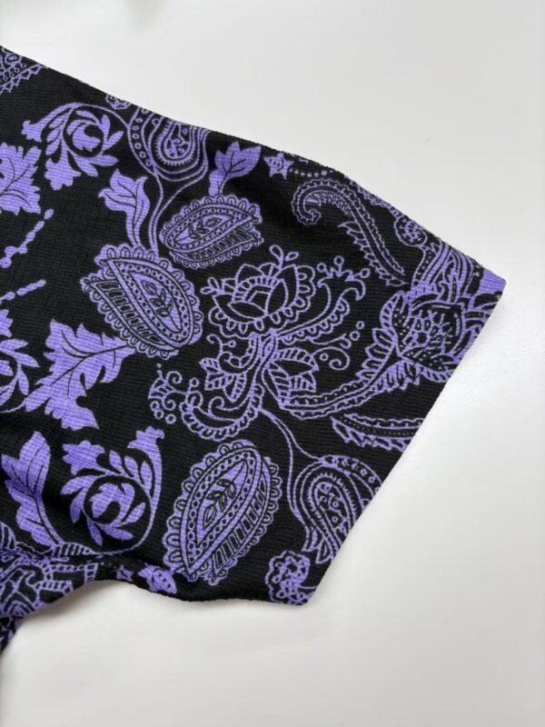 Close-up of black fabric with intricate purple paisley and floral patterns, showcasing detailed textile design for fashion or home decor.
