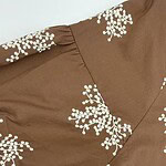 Close-up of a brown dress featuring white floral embroidery, showcasing detailed craftsmanship and stylish design.