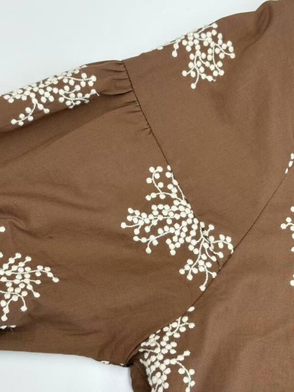 Close-up of a brown dress featuring white floral embroidery, showcasing detailed craftsmanship and stylish design.
