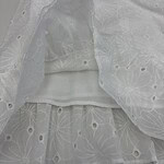 Close-up of white embroidered fabric with floral patterns and eyelet details, ideal for fashion and dressmaking.