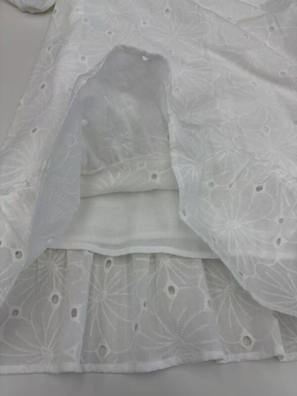 Close-up of white embroidered fabric with floral patterns and eyelet details, ideal for fashion and dressmaking.