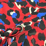 Close-up of a bold animal print fabric with red, black, white, and blue colors, featuring a metal eyelet and seam detail.