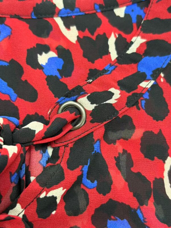 Close-up of a bold animal print fabric with red, black, white, and blue colors, featuring a metal eyelet and seam detail.