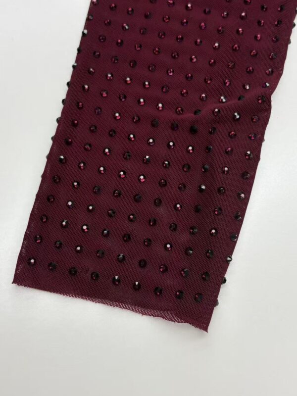 Close-up of burgundy fabric adorned with small black rhinestones, perfect for luxury fashion or evening wear.