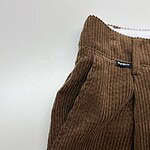 Close-up of brown corduroy pants with a high waist and side pockets, showcasing textured fabric and stylish design.
