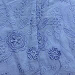Close-up of light blue fabric with intricate floral embroidery and delicate stitching details.