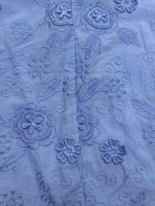 Close-up of light blue fabric with intricate floral embroidery and delicate stitching details.