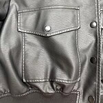 Close-up of a silver leather jacket featuring a front pocket with a snap button and metallic details, perfect for fashion-forward outfits.