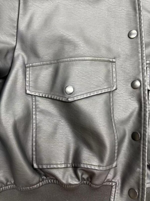 Close-up of a silver leather jacket featuring a front pocket with a snap button and metallic details, perfect for fashion-forward outfits.