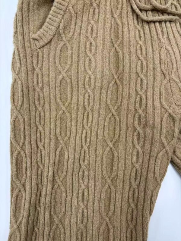 Close-up of beige cable knit sweater pants with intricate pattern and drawstring waist, perfect for casual winter wear.