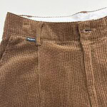 Close-up of brown corduroy pants with front zipper and button, showcasing textured fabric and stylish design.