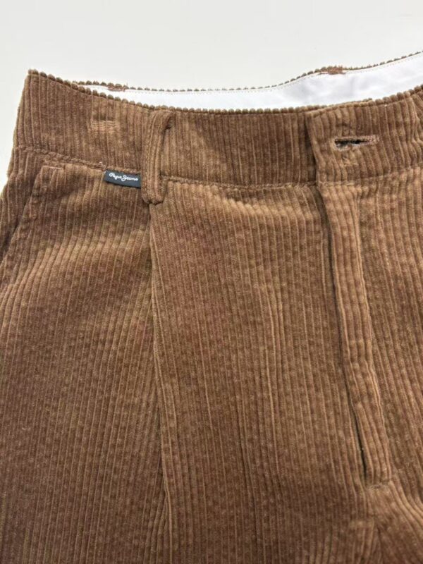 Close-up of brown corduroy pants with front zipper and button, showcasing textured fabric and stylish design.