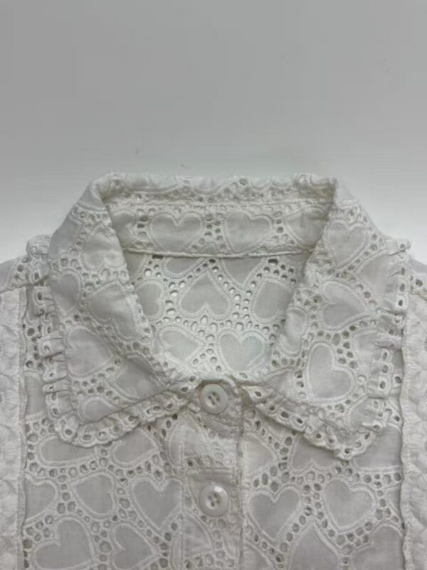 White eyelet lace blouse with heart-shaped patterns and scalloped edges, featuring a collar and button-down front, perfect for stylish casual wear.