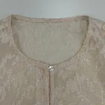 Close-up of a beige lace blouse with a round neckline and pearl button closure, perfect for formal or casual occasions.